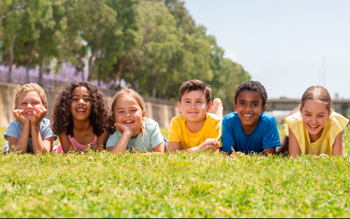 Young children relaxing on a grassy field in the sunshine, representing a secure future, wellbeing, and long-term prosperity.