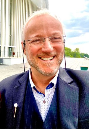 Portrait of Marc in a suit, smiling confidently outside an office building, symbolising trust, expertise, and client-focused service.